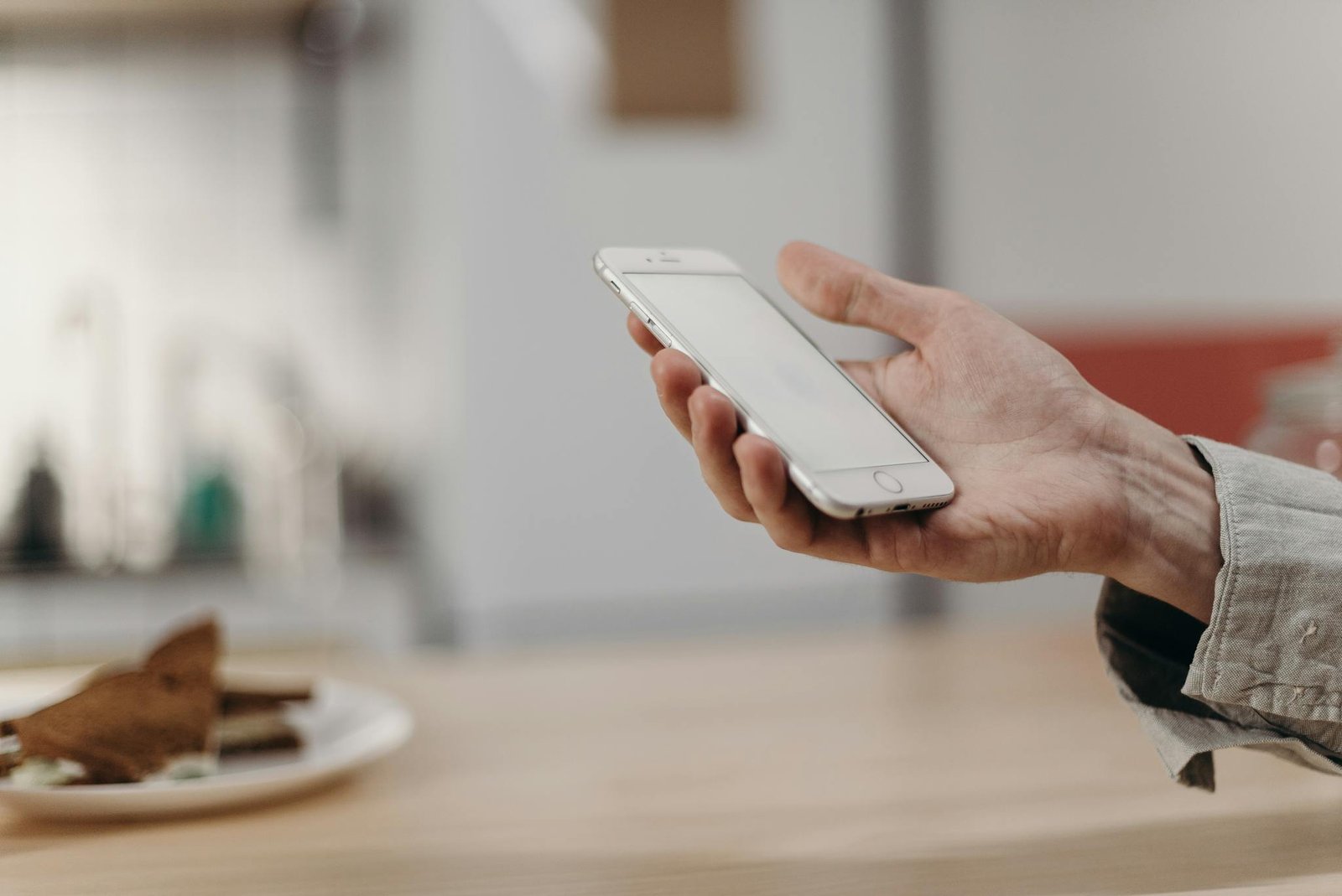 Person holding a smartphone in a cozy modern kitchen, showcasing technology in daily life.